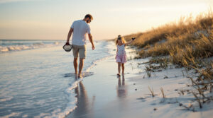 Father and daughter searching for shark teeth on a sandy Gulf Coast beach at sunrise, with gentle waves and grassy dunes in the background.