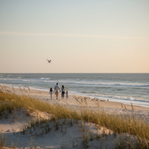 Family walking along a quiet Port St. Joe beach at sunset with dune grasses in the foreground, gentle waves, and shorebirds near the waterline